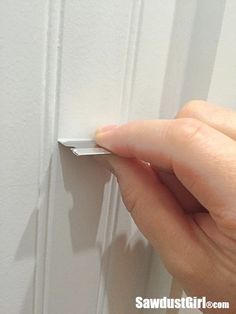 a hand is pulling the corner of a door handle on a white paneled wall