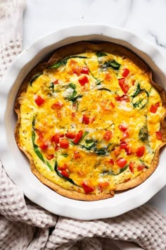 an omelet with tomatoes and spinach in a white dish on a marble surface