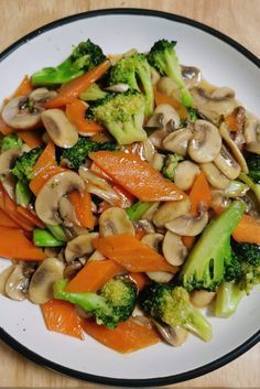 a white plate topped with broccoli, carrots and mushroom stir fry on top of a wooden table