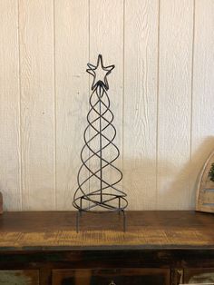 a metal christmas tree sitting on top of a wooden table next to a white wall