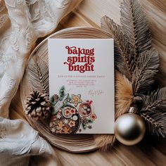 a book sitting on top of a plate next to pine cones and christmas decorations with the title baking spirits bright