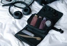 the contents of a travel bag are neatly organized on a bed with white sheets and black headphones