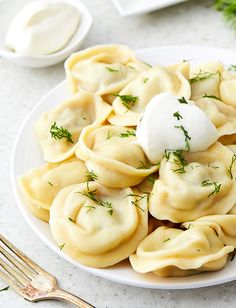 a white plate topped with dumplings covered in sauce and sour cream next to a fork