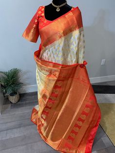 Right in time for Durga Puja, this grand and gorgeous Banarasi semi silk saree pours its richness elegantly through the zari and stone work. The saree is off white shade with golden zari bhuttis and intricate zari work on the pallu and border. Also seen embedded in the saree, are small stones that makes this saree a perfect wear for evening occasions or under the light occasions. Border, blouse and pallu are red shade. Falls and pico are done on the saree. Blouse is fully stitched. Size of the b White Art Silk Pre-draped Saree For Festivals, White Anarkali Set For Diwali, Fitted Pre-draped Saree With Zari Work For Puja, Festive Pre-draped Saree With Mirror Work For Puja, Pre-draped Saree For Puja Festivals, White Pre-draped Saree With Dupatta For Navratri, White Pre-draped Saree With Mirror Work For Eid, White Pre-draped Saree With Mirror Work, Traditional White Blouse Piece With Mirror Work