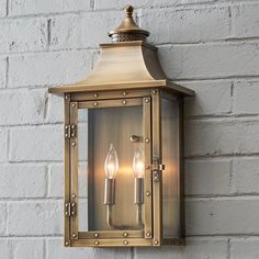 an outdoor wall light with two lights on it's side and brick wall in the background