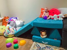 a baby sitting on top of a blue bed surrounded by stuffed animals and other toys