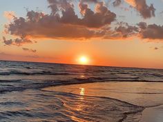 the sun is setting over the ocean with clouds in the sky and water on the beach