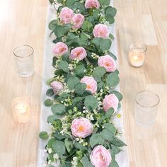 the table is set with pink flowers and greenery on it, along with candles