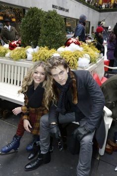 a man and woman sitting on a bench in front of a christmas display at an outdoor event