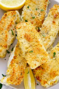 fried fish sticks with lemon wedges and parsley on a white plate, ready to be eaten