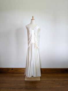 a white dress on a mannequin stand in front of a wall and wooden floor