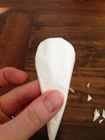 a hand holding a piece of white tissue paper on top of a wooden table next to a knife