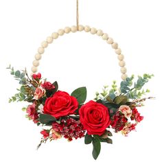 a wreath with red roses and greenery hanging on a string