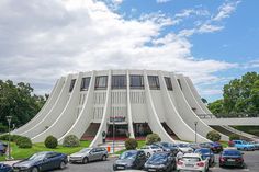 cars are parked in front of a large white building with an unusual design on it