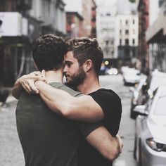 two men embracing each other in the middle of a city street with cars parked on both sides