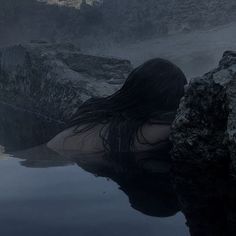 a woman is sitting in the water with her back turned to the camera and she has long black hair