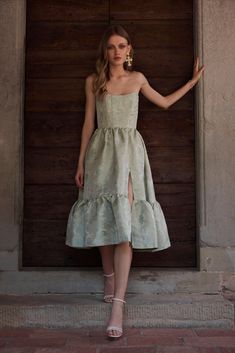 a woman standing in front of a wooden door wearing a dress with ruffles