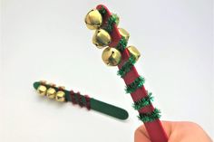 a hand holding a red and green toothbrush with bells on it's end