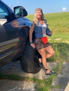 a woman standing next to a truck with her hand on the tire and smiling at the camera