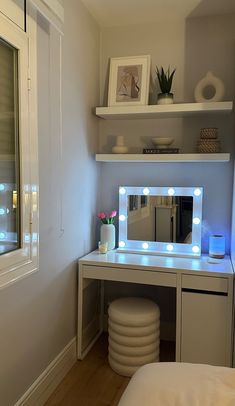 a white desk with lights on it and a mirror in the corner next to a bed