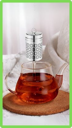 a glass tea pot filled with liquid on top of a wooden coaster