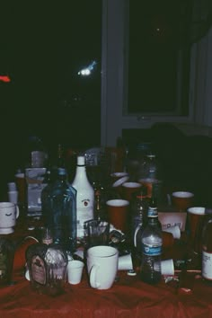 a table topped with lots of bottles and glasses on top of a red cloth covered table