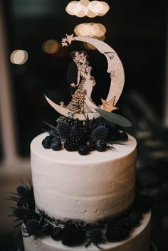 a white cake with black berries on top and a silhouette of a woman sitting on the moon