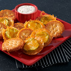 a red plate topped with fried food next to a small bowl of ranch dressing on a black table