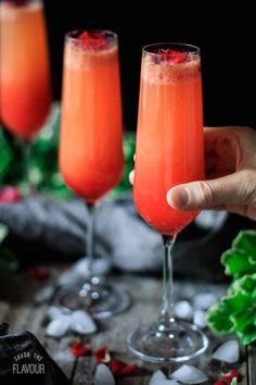 two glasses filled with orange juice and garnished with red berries on the rim