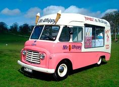 an ice cream truck is parked on the grass in front of a field with trees