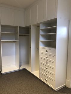 an empty white closet with drawers and shelves on the wall next to carpeted floor