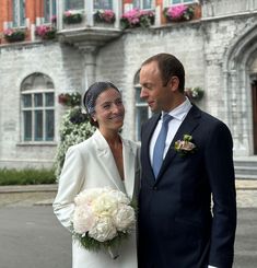 a man and woman standing next to each other in front of a building with flowers on it