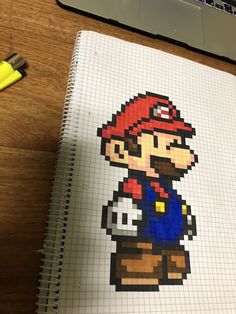 a drawing of mario on a piece of paper next to a pen and laptop computer