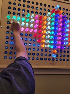 a person points at an array of colored lights on a wall in front of them