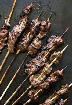 several skewers of meat are being cooked on a grilling pan with chopsticks