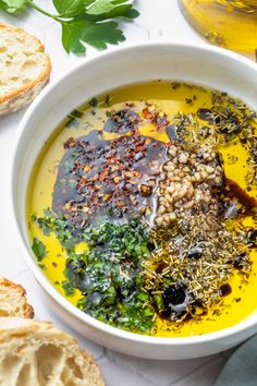 a white bowl filled with yellow soup next to bread and parsley on the side