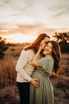 a pregnant woman hugging her husband in an open field at sunset