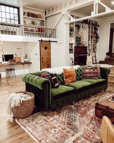 a living room with green couches and rugs in front of a staircase leading up to the second floor