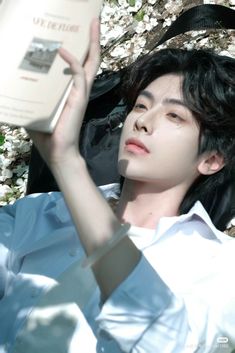 a young man laying on the ground holding an open book in his hand and looking up into the sky