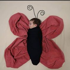 a small child laying on top of a red butterfly shaped bed spread over it's back