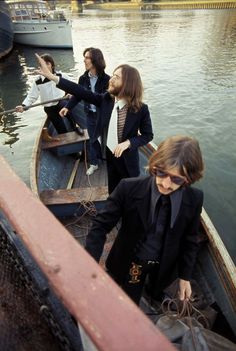 three people on a boat in the water with one pointing at something while another person holds his hand out