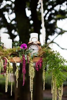 an arrangement of flowers and candles hanging from a wooden beam in front of a tree