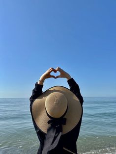 a woman standing on top of a beach next to the ocean holding her hands in the air