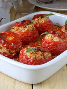 tomatoes stuffed with rice and herbs in a white casserole dish on a wooden table