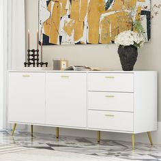 a large painting hangs on the wall above a white cabinet with gold handles and drawers