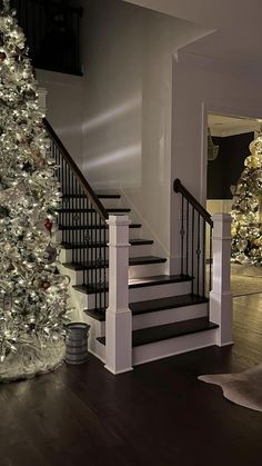 a decorated christmas tree sitting in the middle of a living room next to a stair case