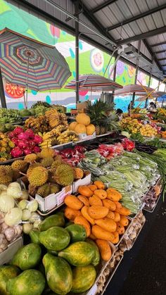 there are many different types of fruits and vegetables on display in the market area with umbrellas over them