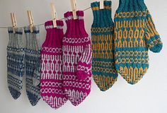 three knit mittens hanging from clothes pins on a line in front of a white wall