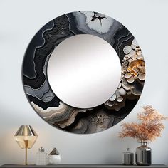 a round mirror sitting on top of a table next to a lamp and vase filled with flowers