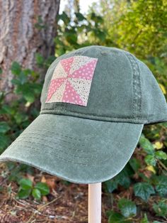 a green hat with pink patchwork on it sitting next to a tree in the woods